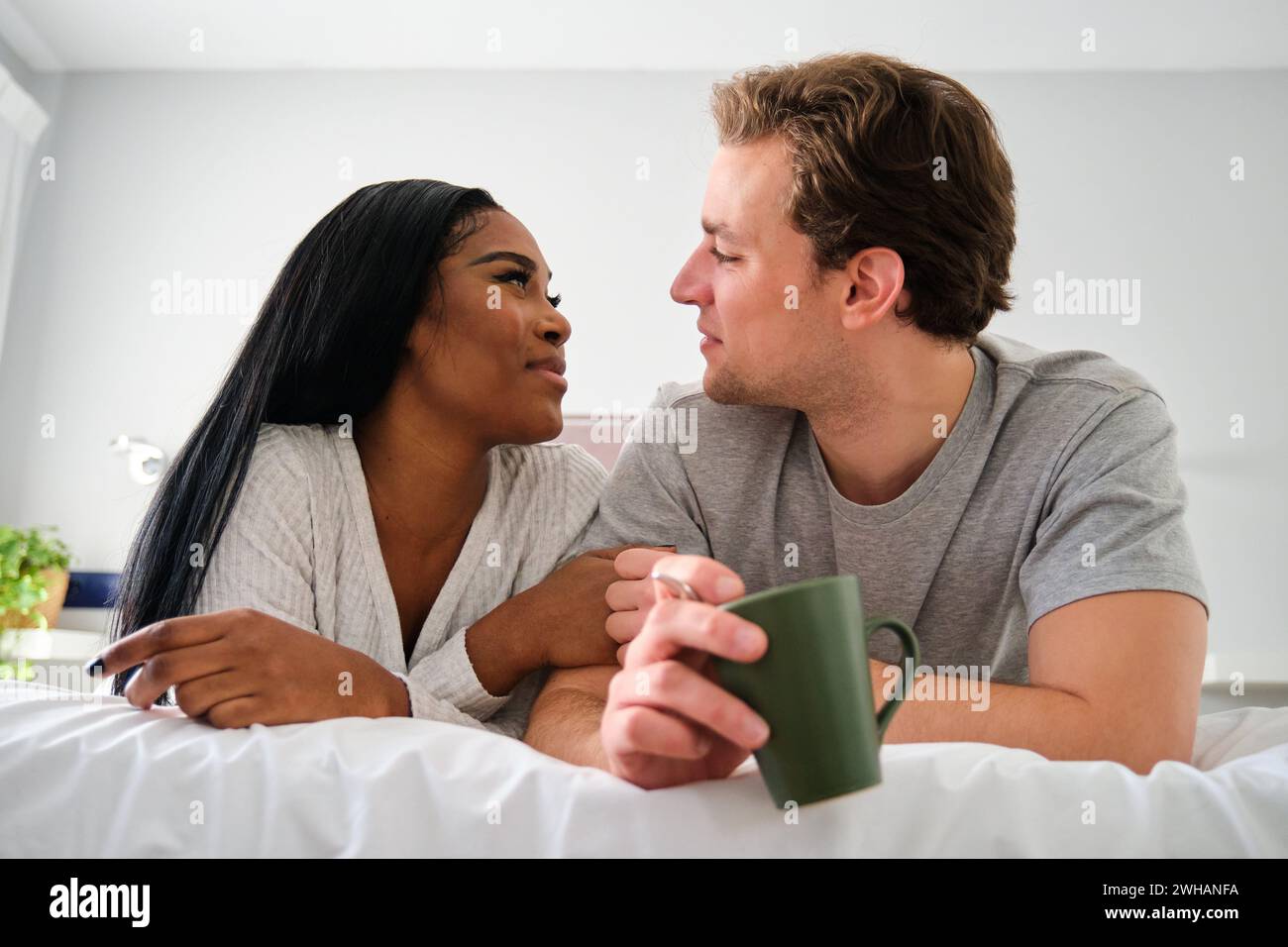 Ein multiethnisches Paar, das sich ansieht und im Bett lächelt. Stockfoto