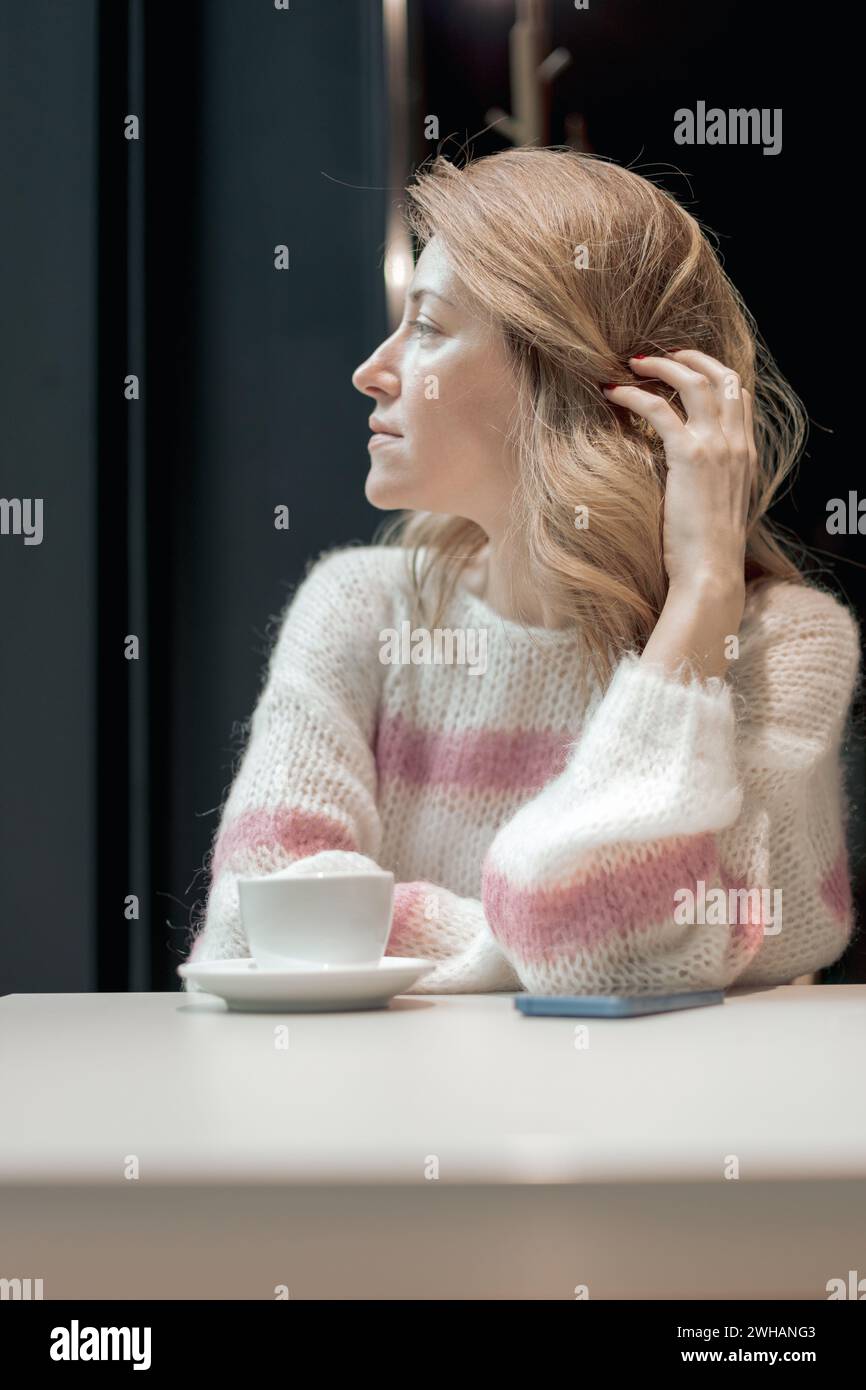 Frau, die mit einer Tasse Kaffee am Tisch wartet Stockfoto