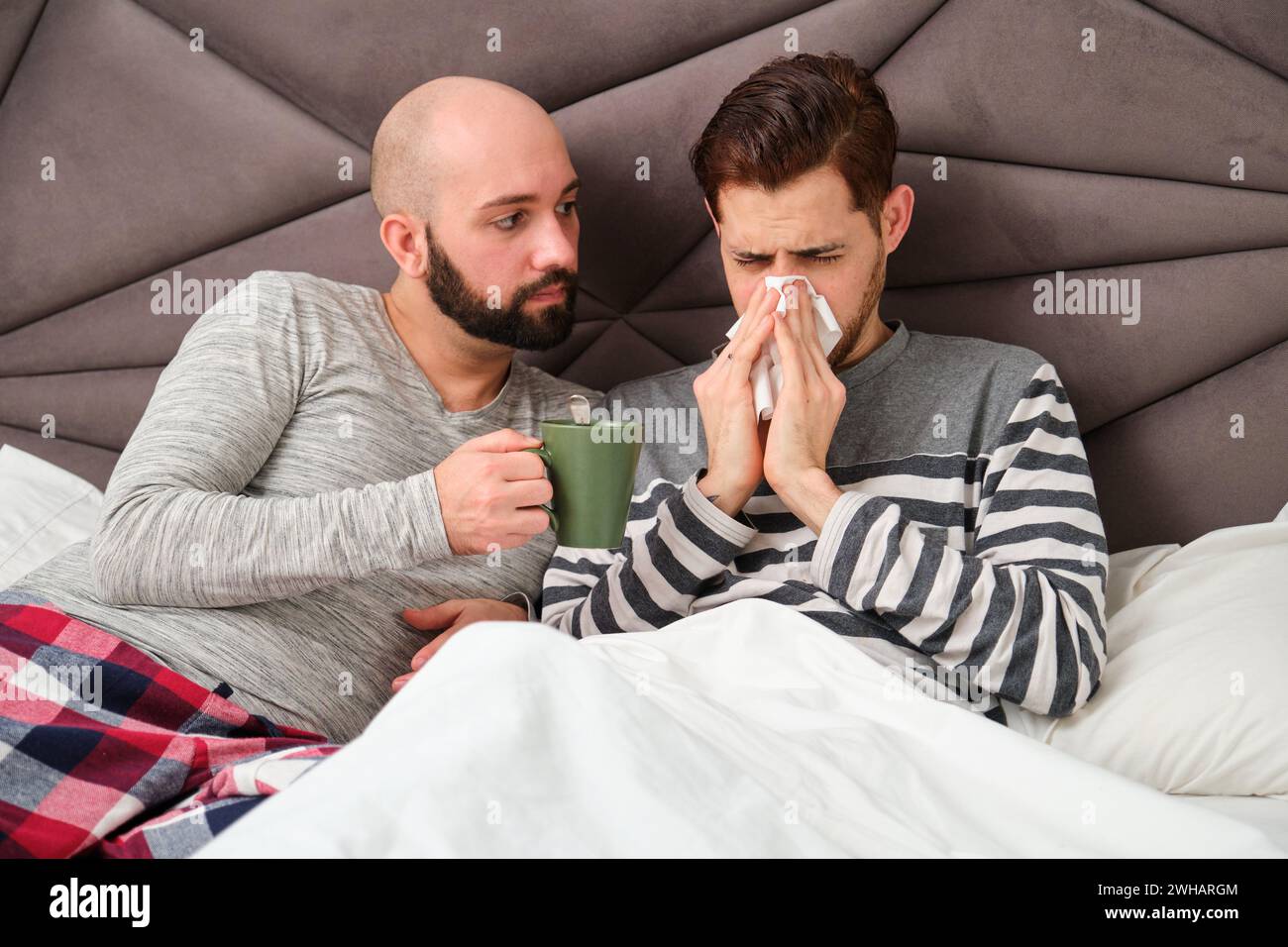 Ein Mann, der sich die Nase in ein Taschentuch bläst, während sein Freund sich um ihn kümmert. Stockfoto