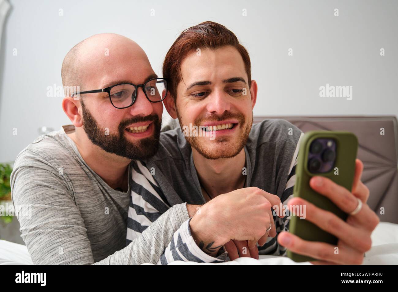 Homosexuelles glückliches Paar, das das Telefon zusammen im Bett benutzt. Stockfoto