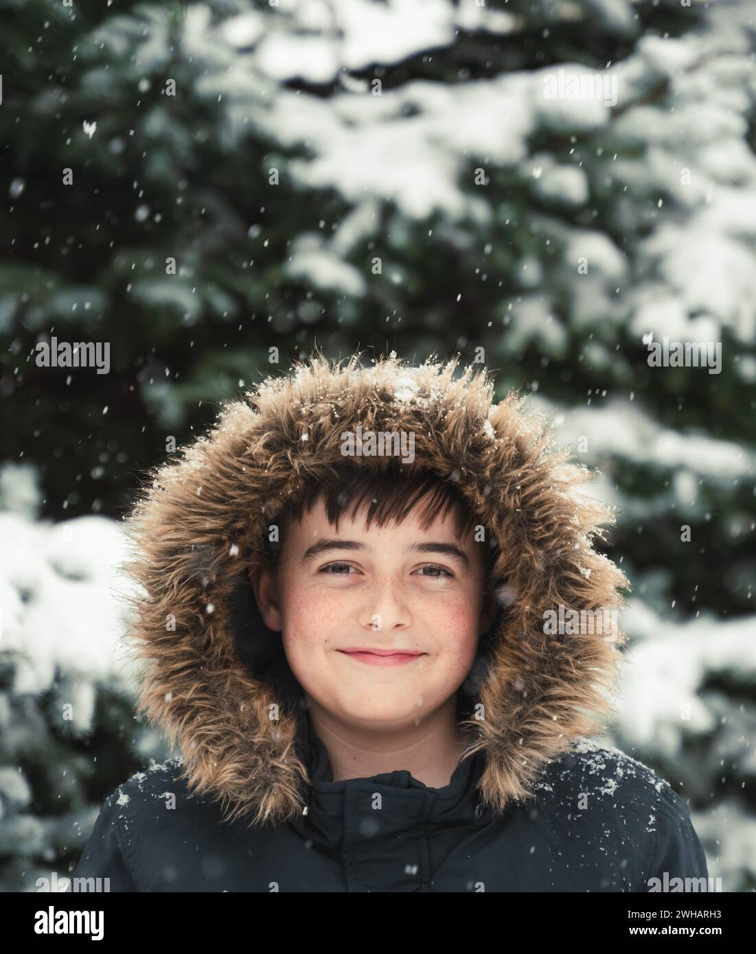 Happy Boy trägt Mantel mit Pelzhaube draußen im Schnee am Wintertag. Stockfoto