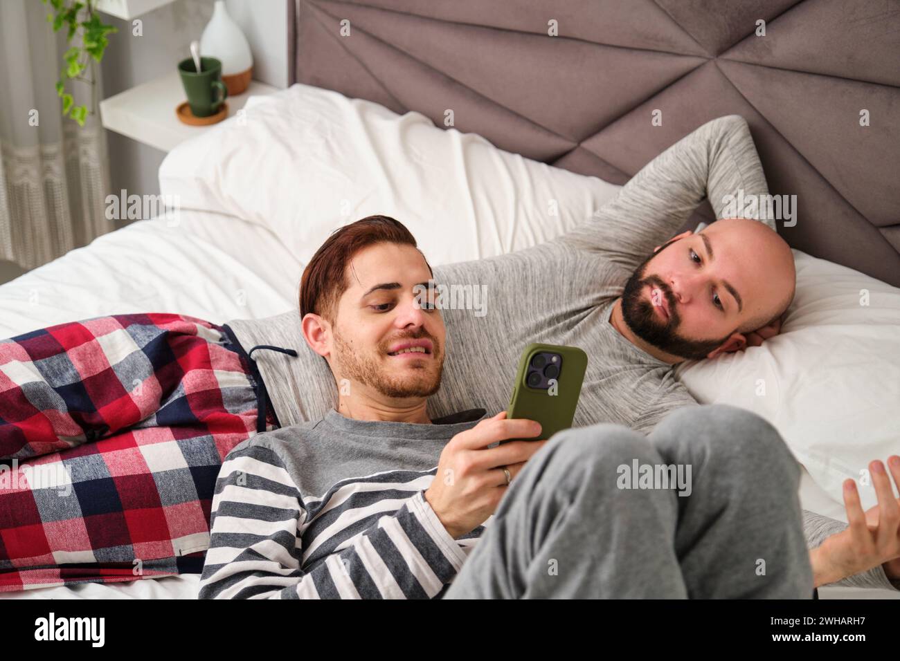 Homosexuelles Paar, das gemeinsam das Telefon benutzt und sich im Bett entspannt. Stockfoto
