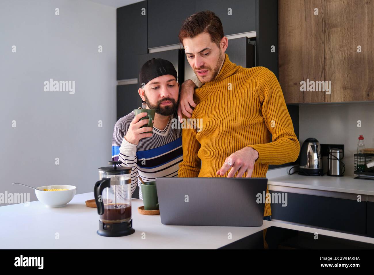 Homosexuelles Paar, das den Laptop benutzt und beim Frühstück redet. Stockfoto