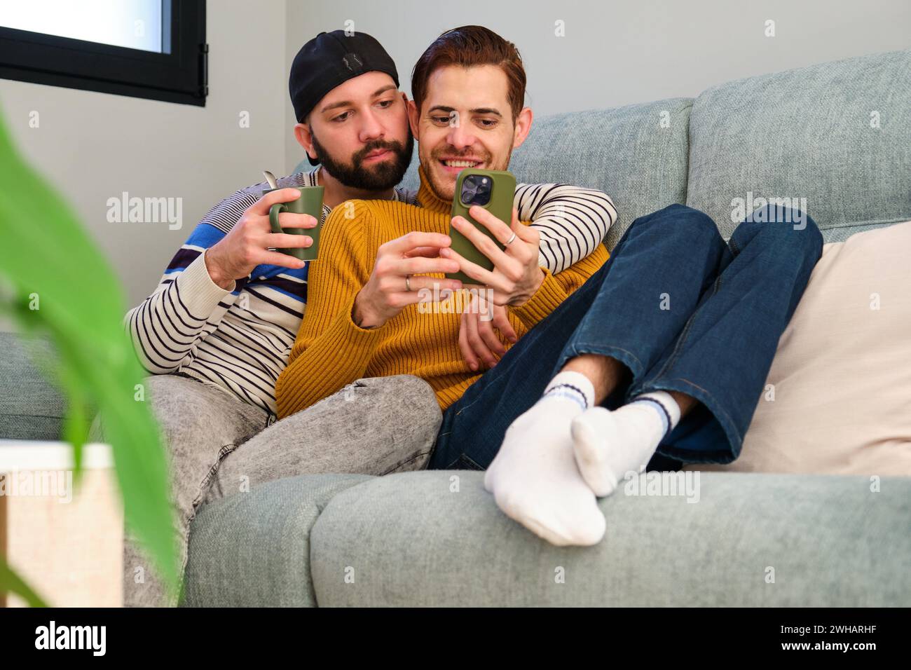 Homosexuelles Paar, das auf dem Sofa liegt und gemeinsam das Telefon benutzt. Stockfoto