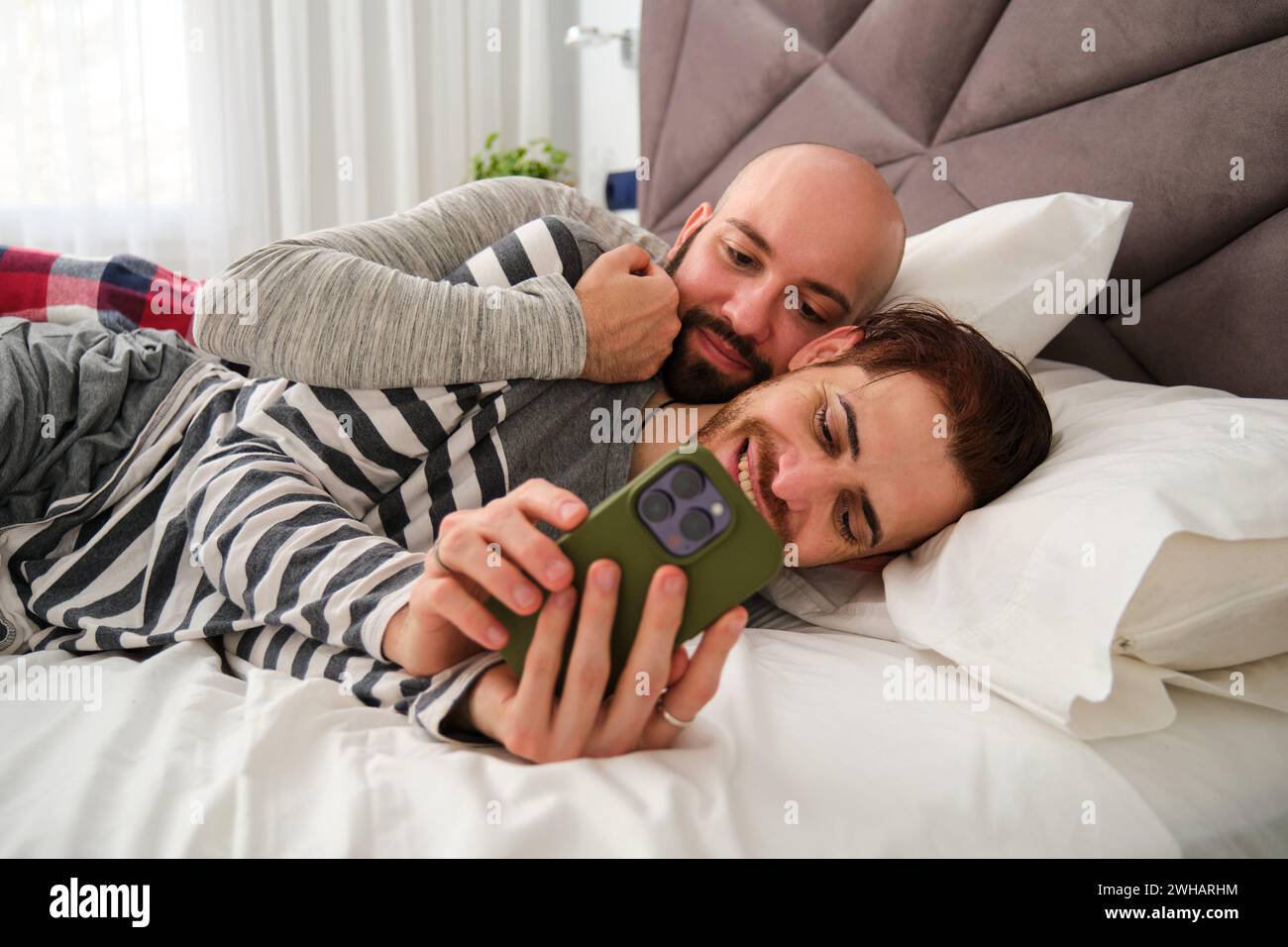 Schwule glückliche Paare, die das Telefon zusammen im Bett benutzen. Stockfoto