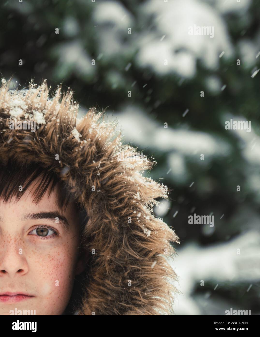 Nahaufnahme eines Jungen mit Pelzhaube draußen im Schnee am Wintertag. Stockfoto