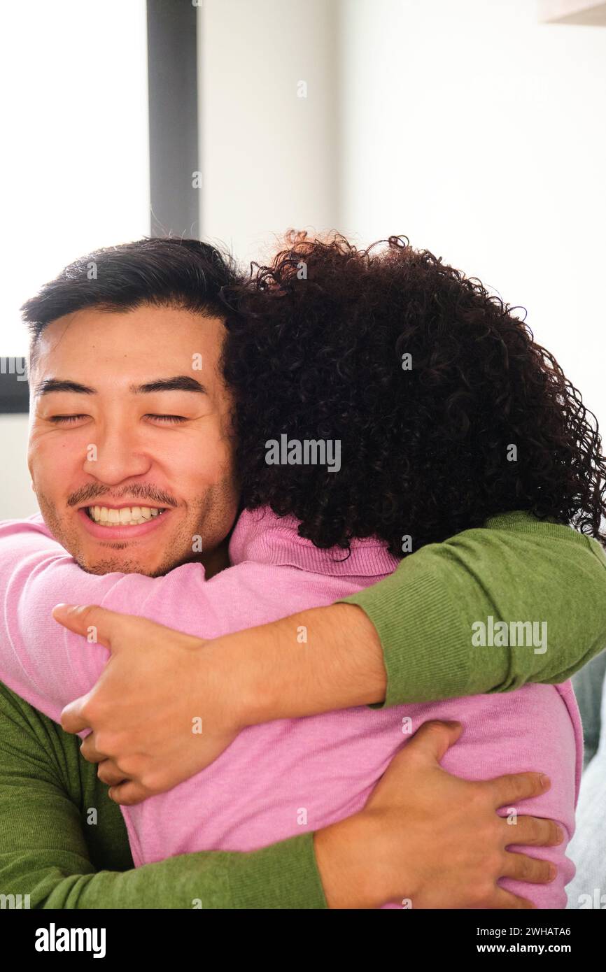 Asiatischer Mann umarmt seine lateinische Freundin zu Hause. Stockfoto