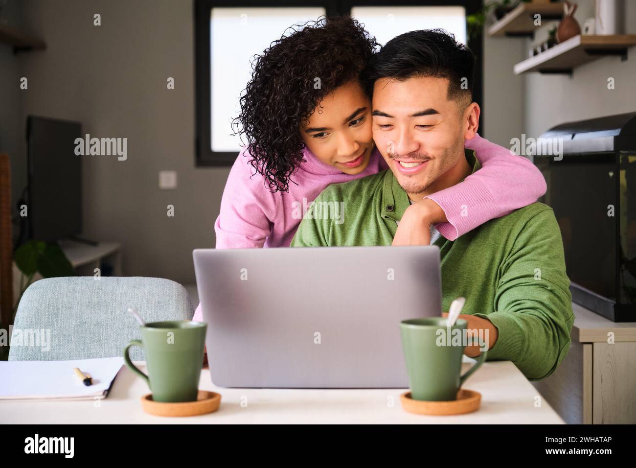Multirassisches Paar lächelt mit dem Laptop und umarmt sich. Stockfoto