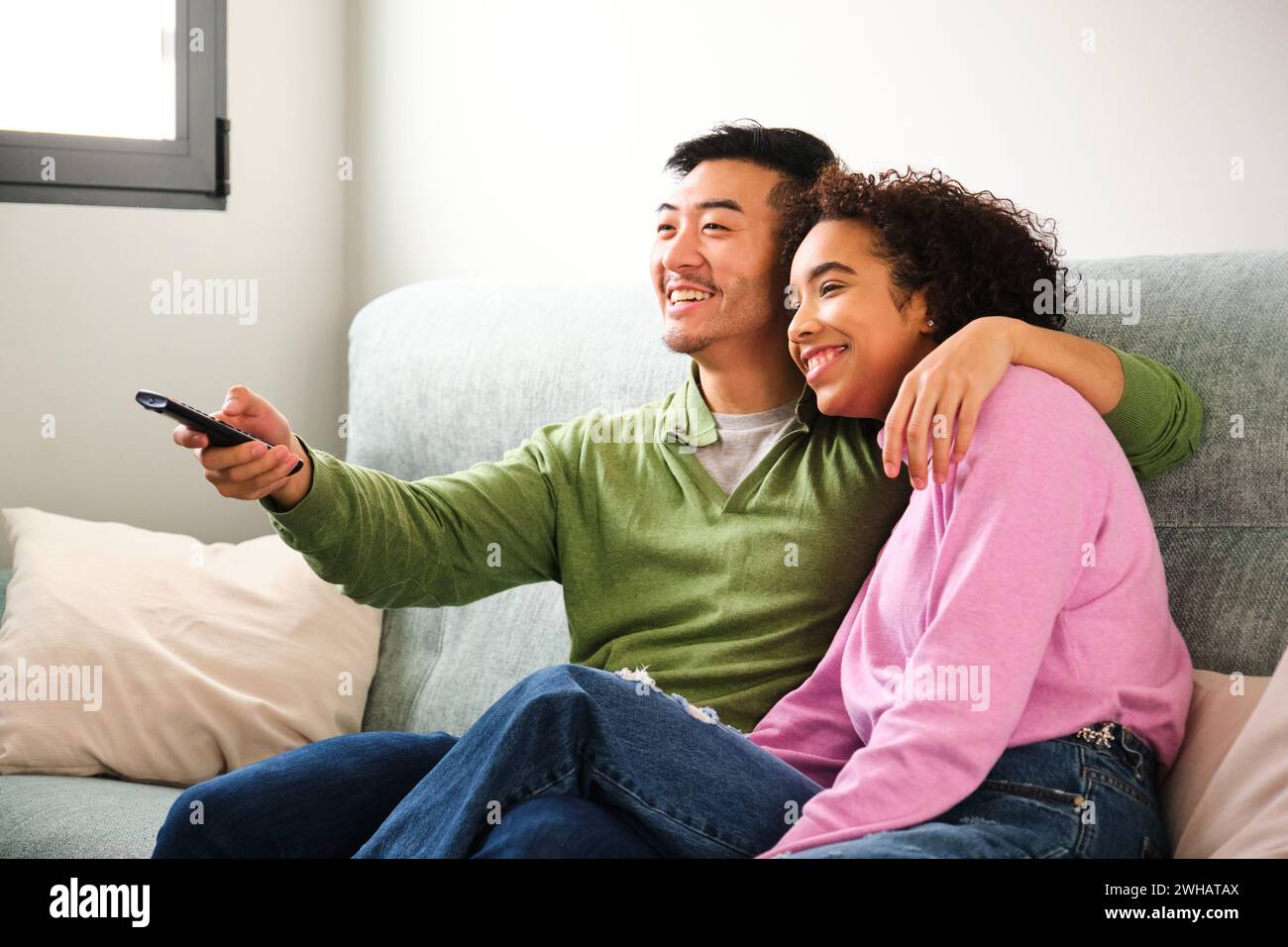 Multiethnische glückliche Paare, die gemeinsam auf dem Sofa Fernsehen, Filme oder Filme sehen. Stockfoto
