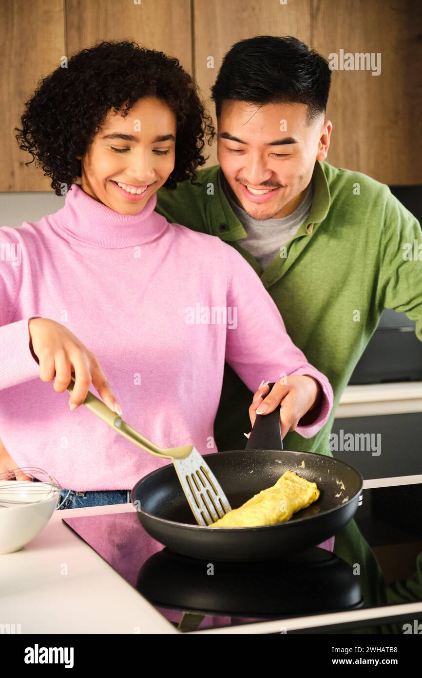 Multiethnische Paare kochen Omelette zusammen in der Küche. Stockfoto