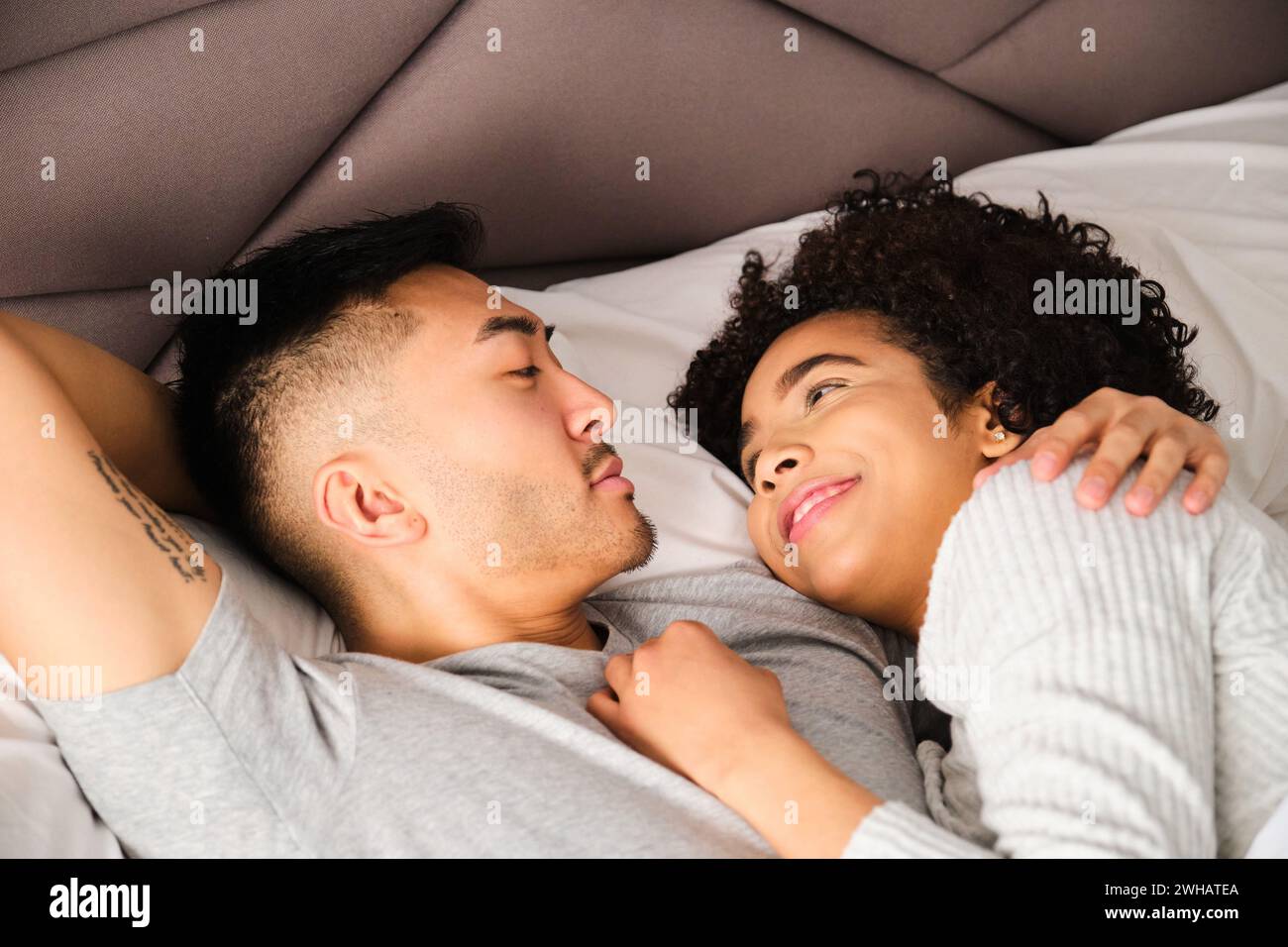 Multiethnische Paare sehen sich im Bett liebevoll aus. Stockfoto