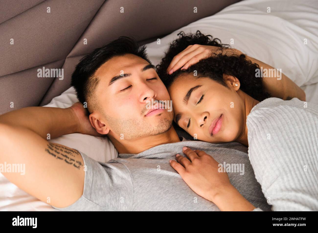 Multiethnisches glückliches Paar, das umarmt auf dem Bett schläft. Stockfoto