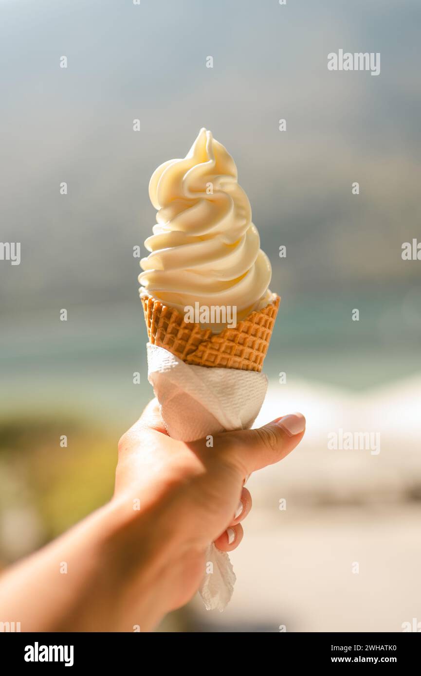 Hand hält Vanilleeis in einem Kegel vor dem Hintergrund des Strandes Stockfoto