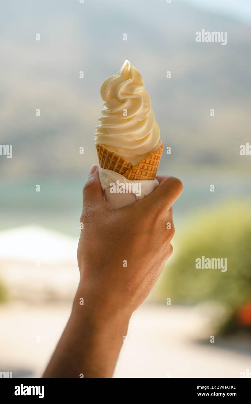 Hand hält Vanilleeis in einem Kegel vor Naturhintergrund Stockfoto