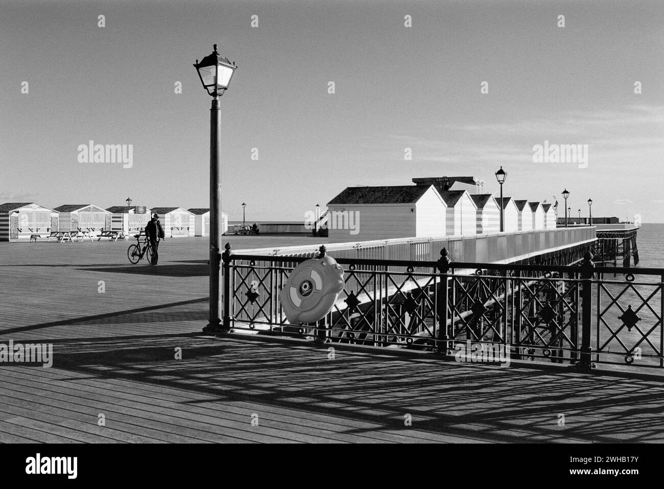 Hastings Pier, East Sussex, UK, in Schwarzweiß, mit Strandhütten, bei Sonnenschein Stockfoto