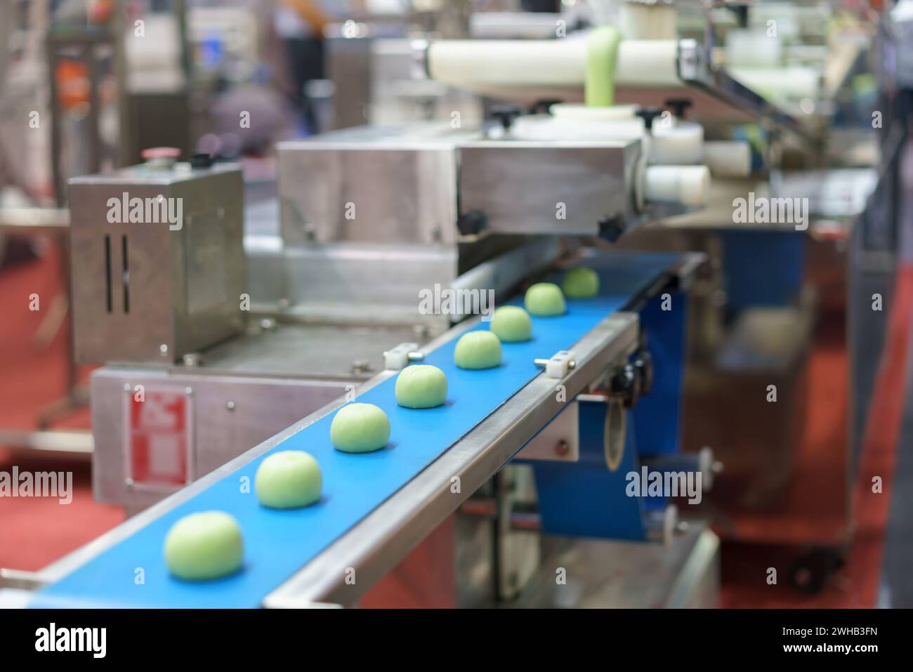 Nahaufnahme einer automatisierten industriellen Lebensmittelverarbeitungsanlage, die Teigportionen auf einem blauen Förderband zeigt, mit Maschinenelementen im Backgr Stockfoto