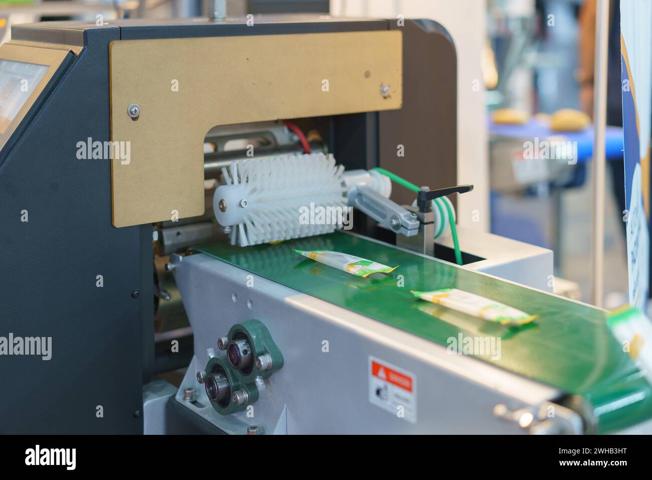 Nahaufnahme einer automatisierten Verpackungsmaschine im Betrieb, Verschließen von Snackpaketen auf einem grünen Förderband, mit mechanischen Komponenten in VI Stockfoto
