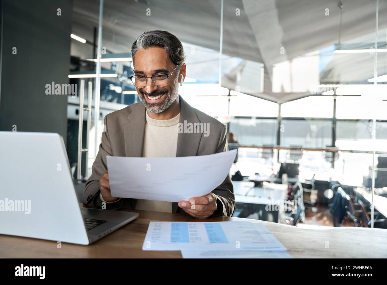 Glücklicher Geschäftsmann mittleren Alters, der sich mit einem Notebook-Hybrid beschäftigt, der im Büro arbeitet. Stockfoto