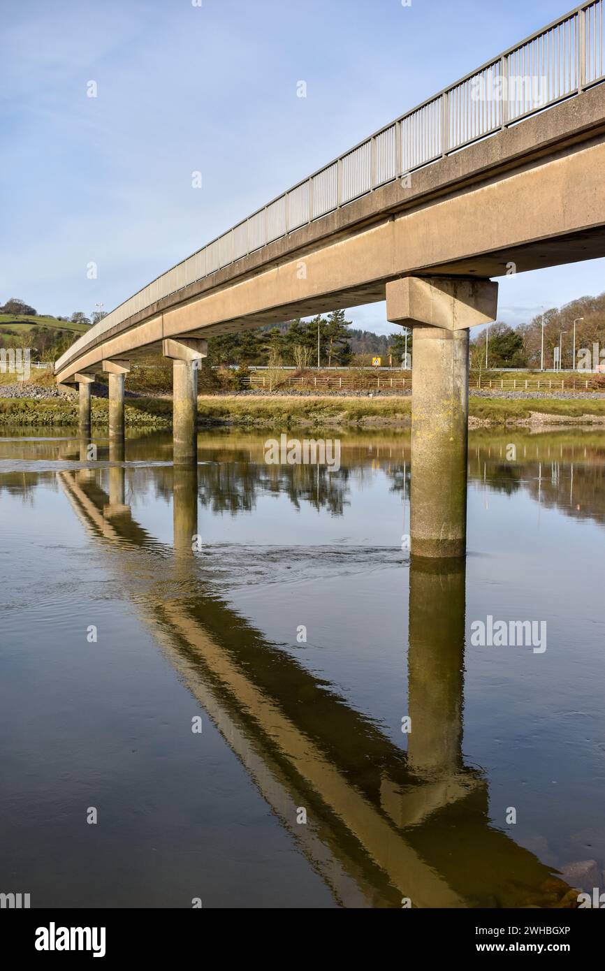 Eine Fußgängerbrücke aus Beton, die einen Fluss überquert und auf der Wasseroberfläche reflektiert. Stockfoto