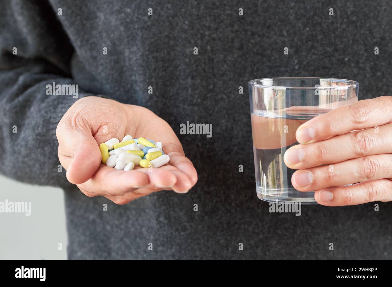 Aufnahme einer nicht erkennbaren Hand eines jungen Mannes, der viele Pillen und ein Glas Wasser zeigt Stockfoto