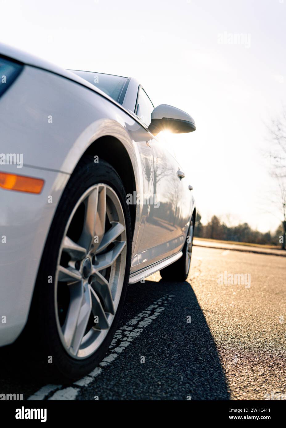 Niedriger Winkel eines weißen Autos mit Hintergrundbeleuchtung, die Sonne über dem Rückspiegel scheint Stockfoto