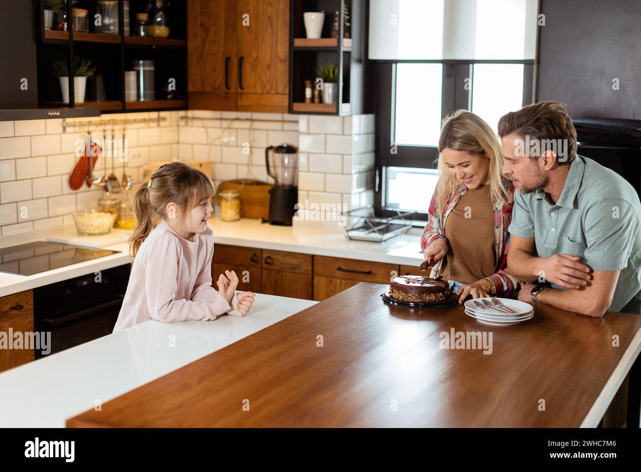 Eine herzerwärmende Szene entfaltet sich, während eine Familie einen köstlichen Schokoladenkuchen zusammen in der Wärme ihrer sonnendurchfluteten Küche genießt und Lächeln und cr teilt Stockfoto