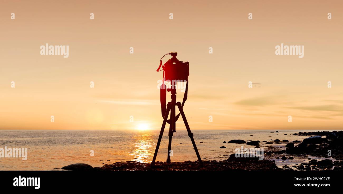 Fotokamera mit Stativ vor einem Sonnenuntergang am Meer Stockfoto