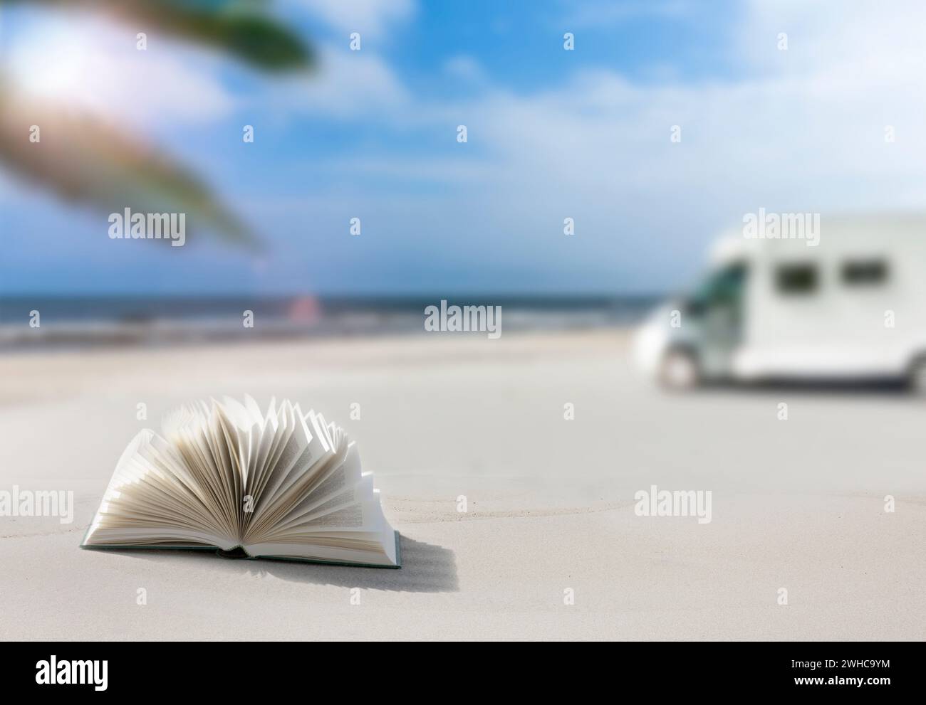 Wohnmobil an einem Sandstrand mit verschwommenem Hintergrund, Buch im Vordergrund Stockfoto