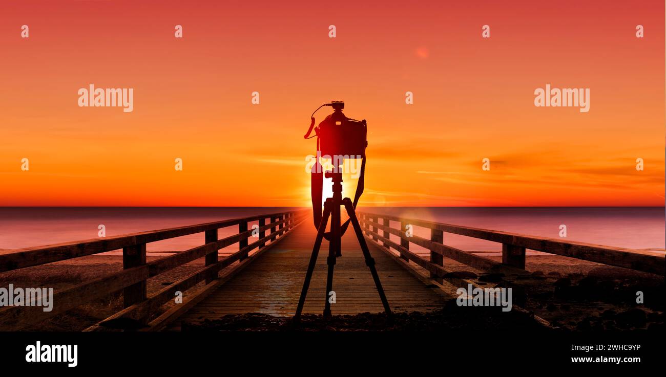 Fotokamera mit Stativ vor einem Sonnenuntergang am Meer Stockfoto