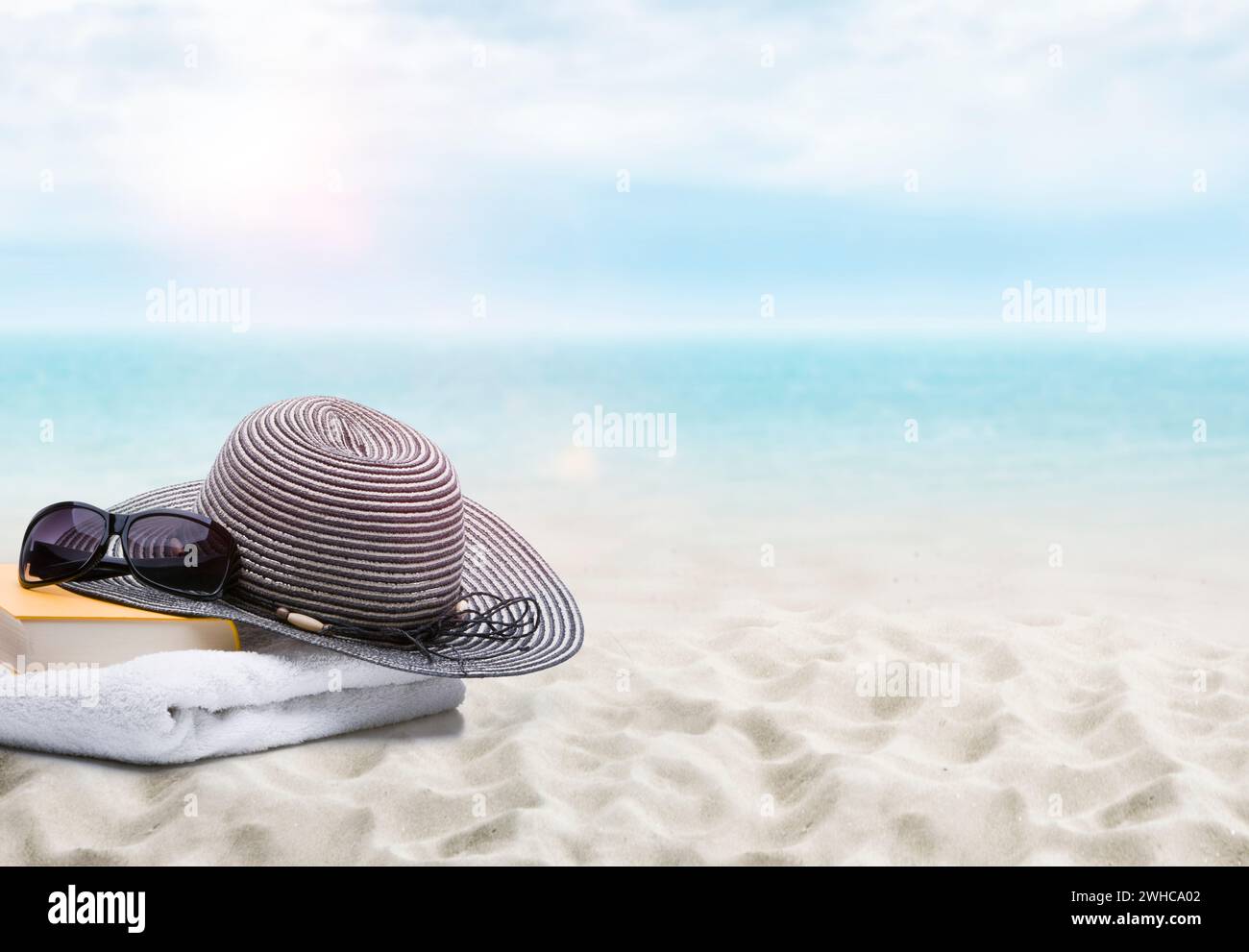 Buch, Sonnenbrille, Handtuch und Sonnenhut am Sandstrand Stockfoto