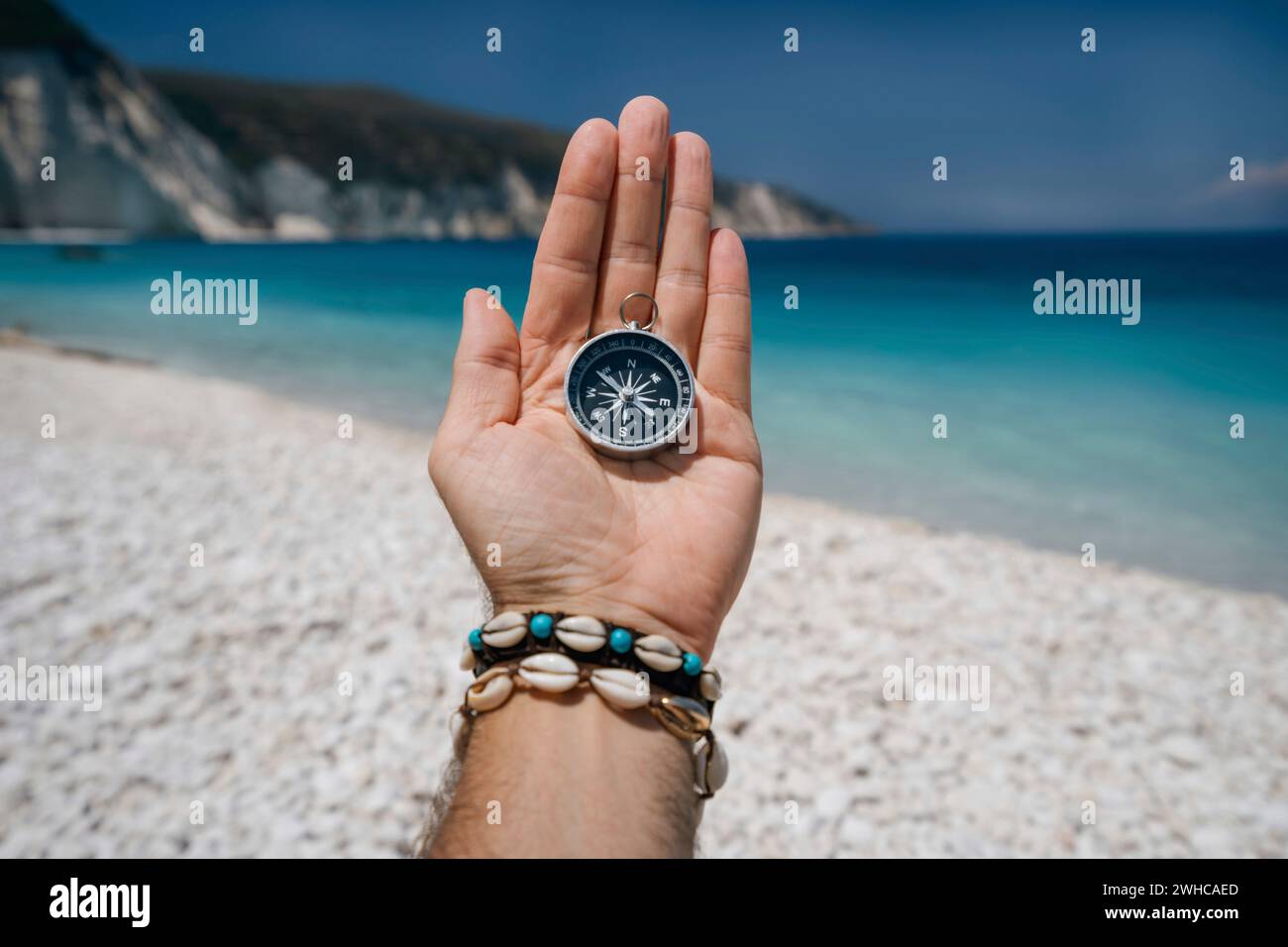 Hand hält einen Kompass auf dem Strand im Hintergrund. Stockfoto