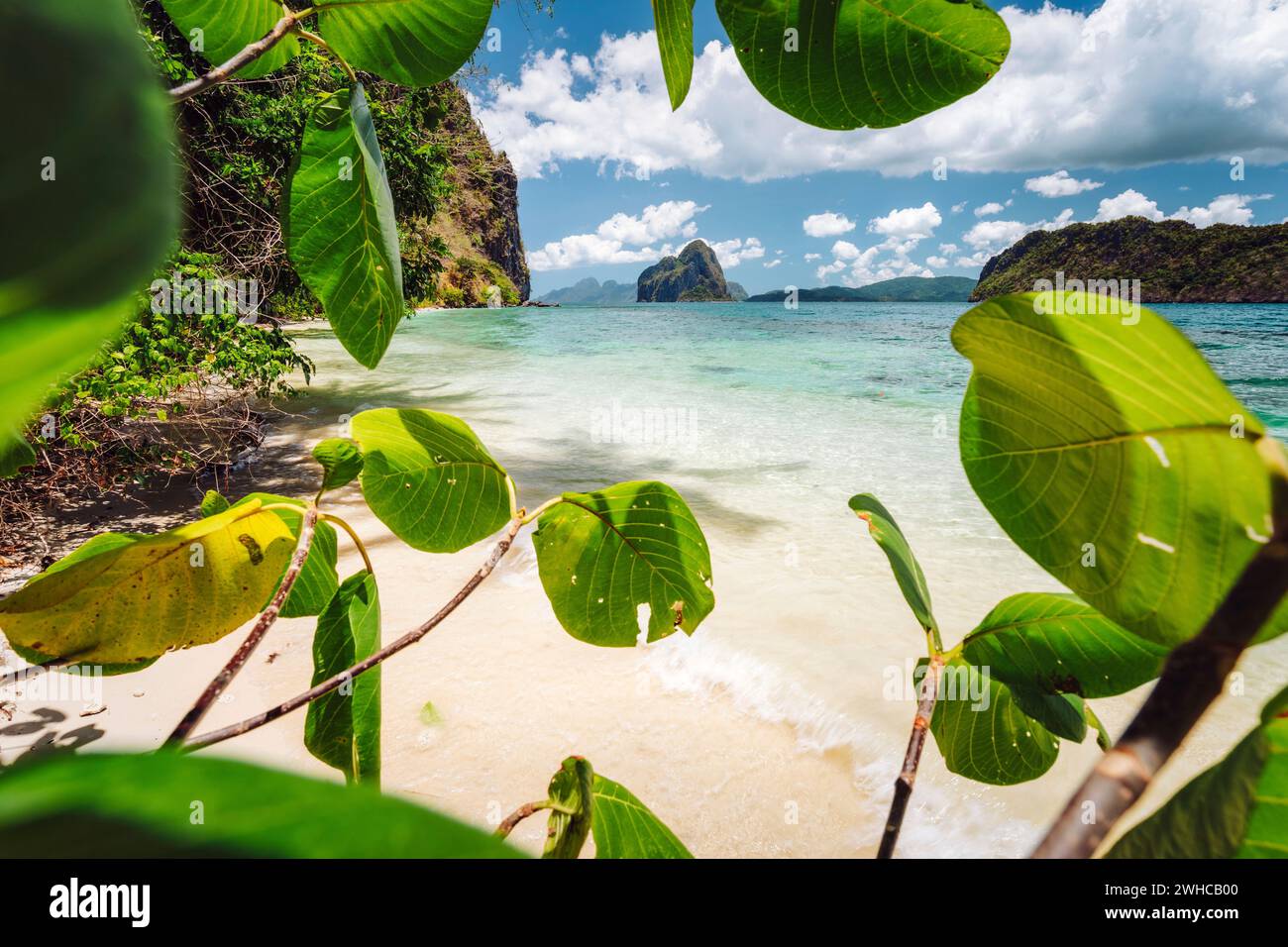 Philippinen, Palawan. Urlaubsszene mit tropischer Strandlandschaft mit felsigen Inseln und beeindruckenden Wolken, umgeben von üppiger Vegetation. Stockfoto