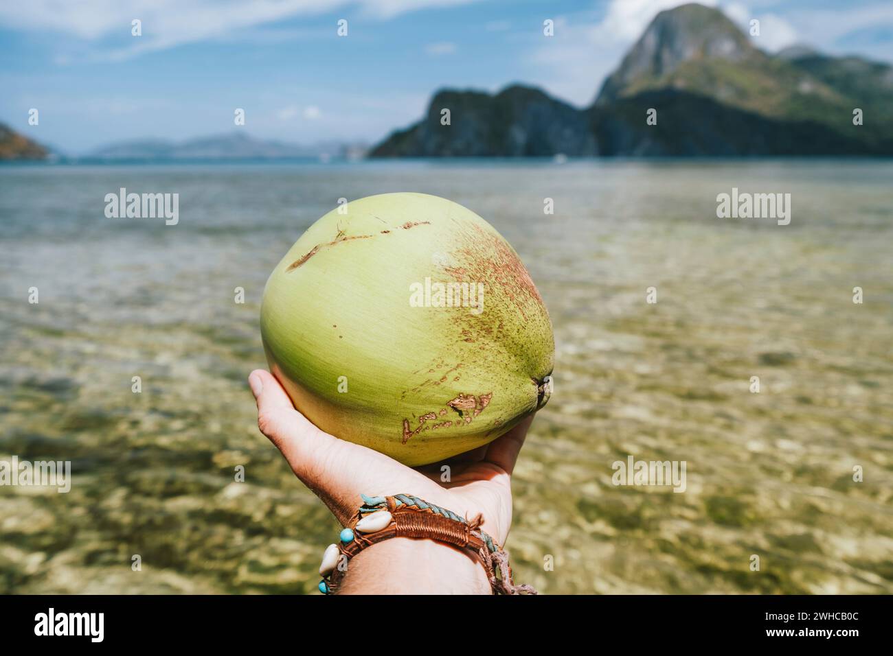 Kokosnuss in männlichen Händen gegen exotische Ozeaninseln. Stockfoto