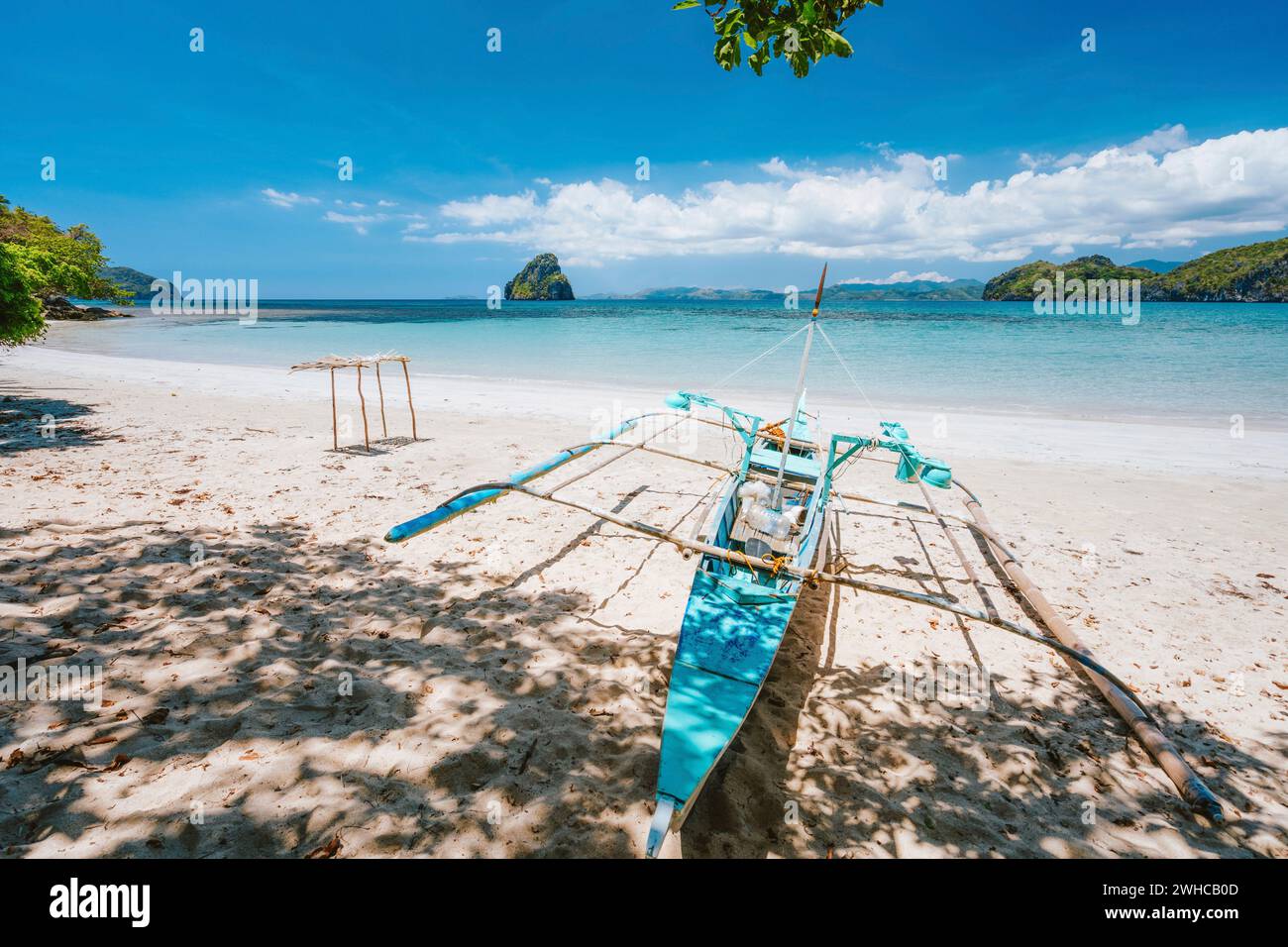 Urlaubsvibes. Traditionelle Fischer banca Boot am sandigen, leeren tropischen Strand. Blaue Ozeanlagune im Hintergrund. El Nido, Philippinen. Stockfoto