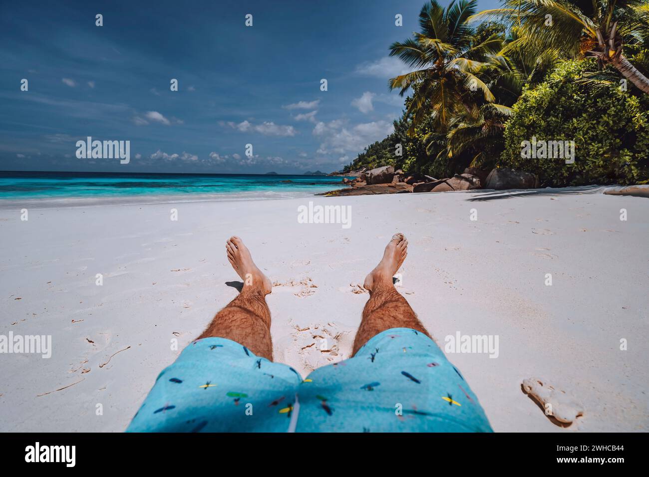 Männer tragen Badeshorts mit gebräunten Beinen am paradiesischen weißen Sand tropischen exotischen Strand mit Blick auf türkisblauem Meer. Reiseurlaub Urlaubskonzept. Stockfoto