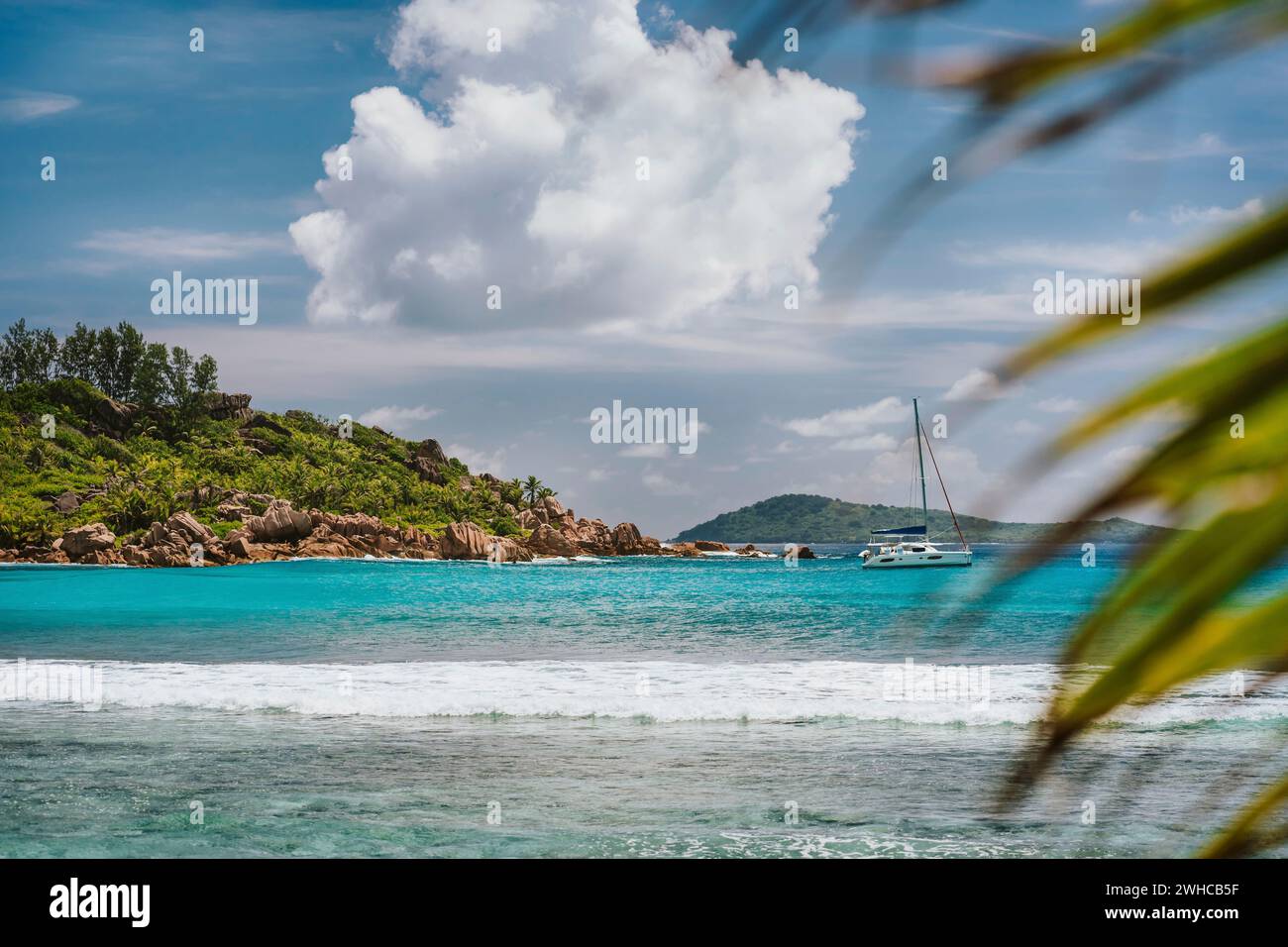 Blaue, flache Lagune, weiße Ozeanwelle und einsames Yachtboot am Strand von Anse Cocos, La Digue Island, Seychellen. Luxusreiseziel. Stockfoto