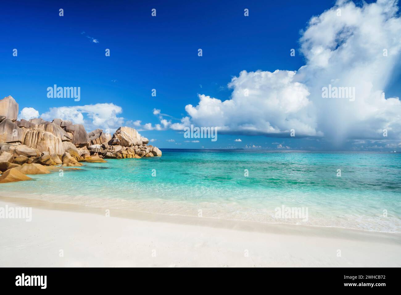 Heller sonniger Tag am großen Anse-Strand auf der Insel La Digue auf den Seychellen. Sandstrand mit blauer Meeresbucht, weiße Wolken im Hintergrund. Stockfoto