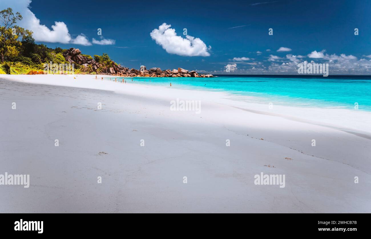 Exotischer Sandstrand von Grand Anse auf der Insel La Digue auf den Seychellen. Unerkannte Touristen schwimmen und entspannen in der blauen Lagune im Hintergrund. Stockfoto