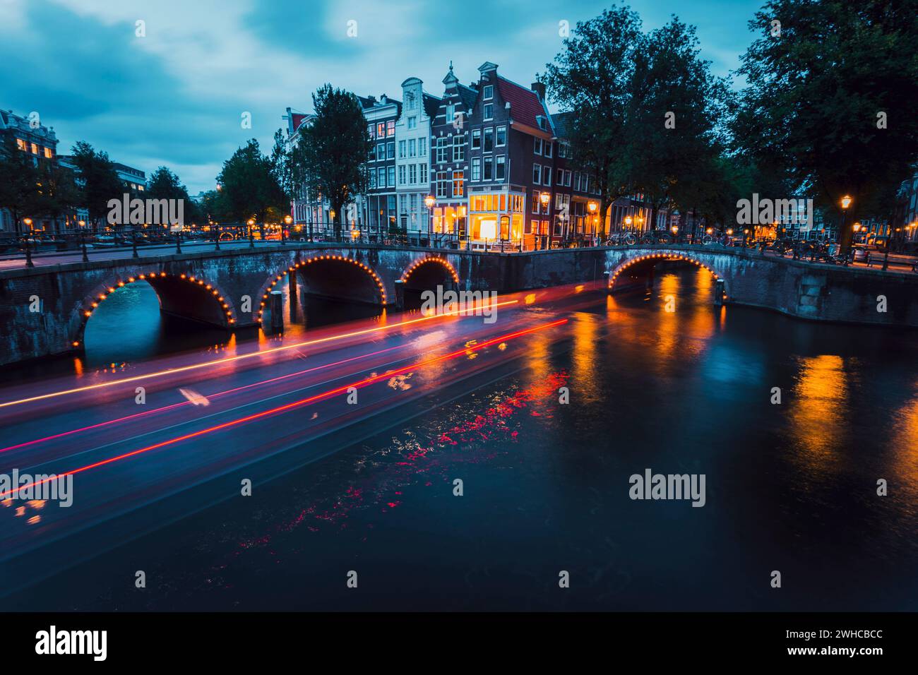Fantastische Lichtwege und Reflexionen auf dem Wasser an den Kanälen Leidsegracht und Keizersgracht in Amsterdam am Abend. Langbelichtungsaufnahme. Romantisches Städtetrip-Konzept. Stockfoto