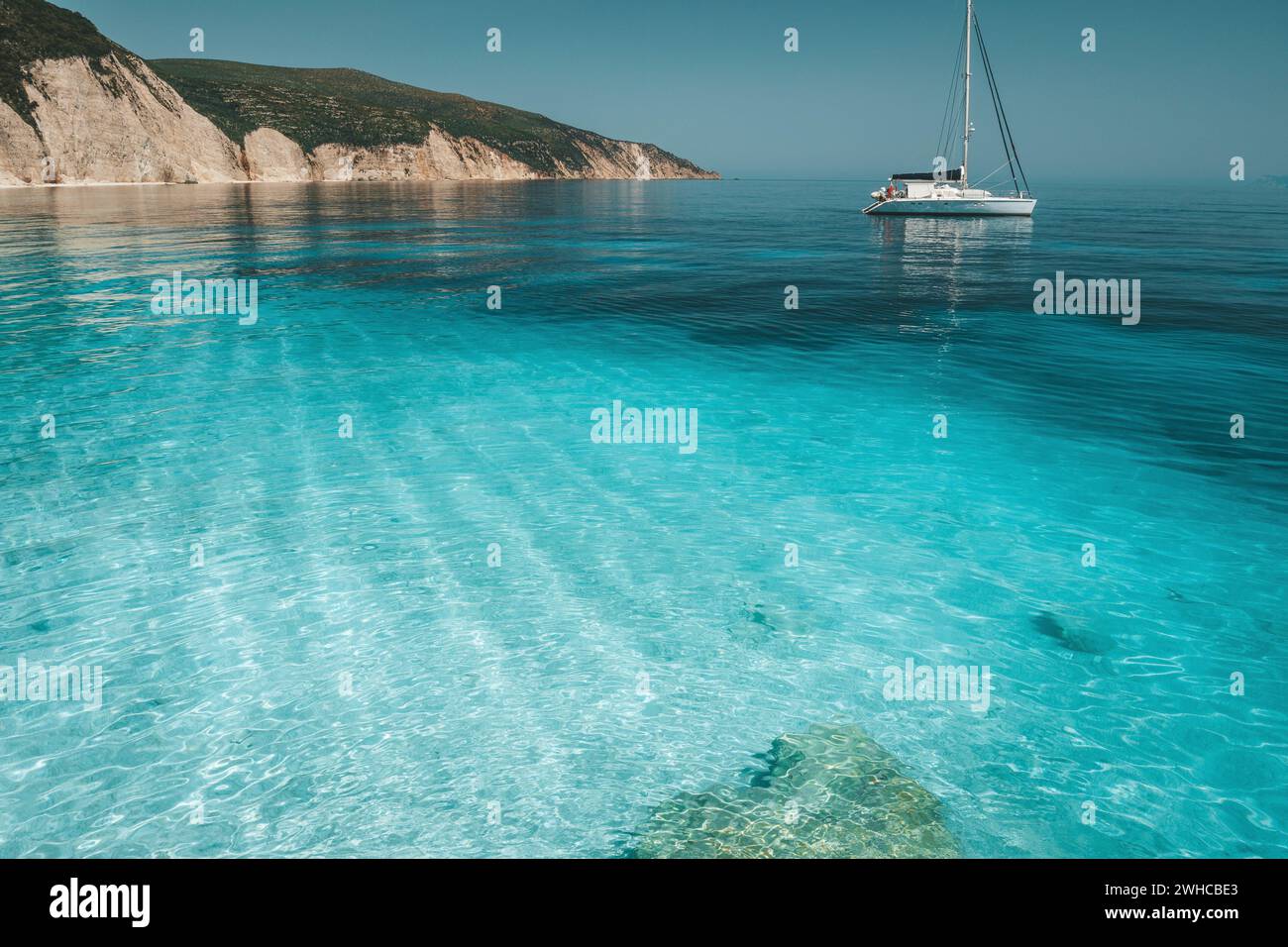 Azure Blue Lagoon mit ruhigen Wellen und die Abdrift segeln Katamaran Yacht Boot. Felsige Steilküste im Hintergrund. Stockfoto