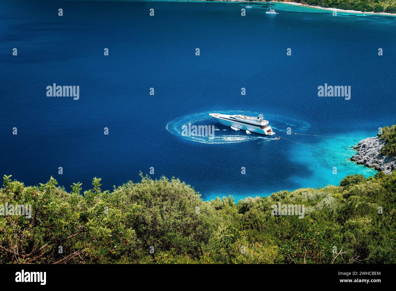 Luxuriöses weißes Segelboot vor Anker in einer ruhigen Bucht im tiefblauen Wasser, in der Nähe der malerischen Küste griechischer Inseln. Stockfoto