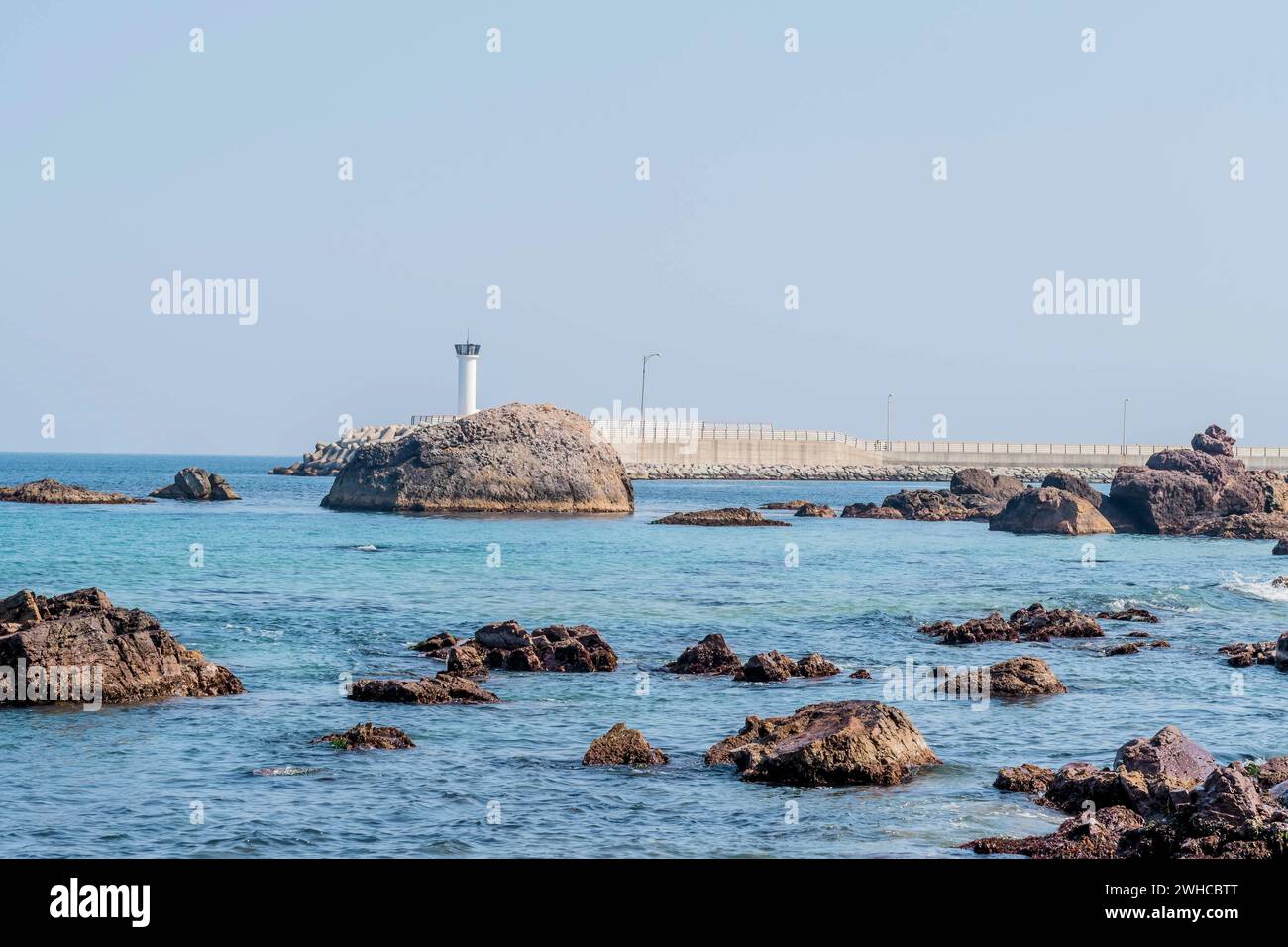 Große Felsbrocken im Ozean vor dem weißen Leuchtturm auf Betonpier Stockfoto