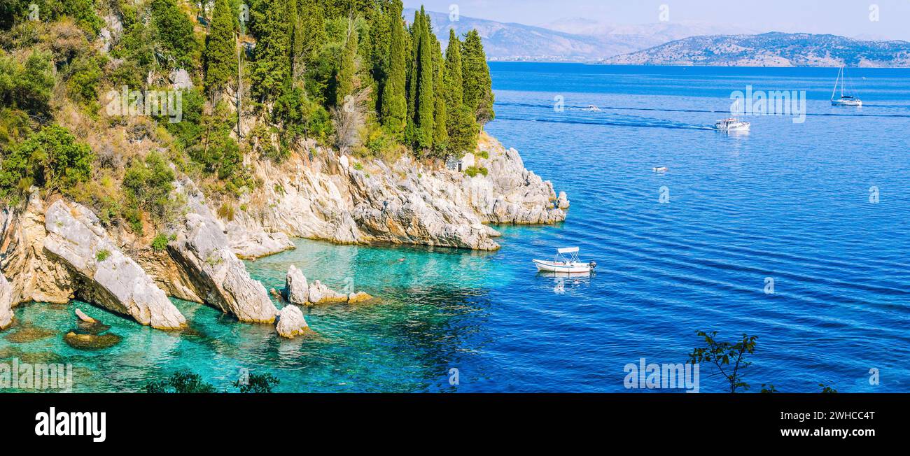 Felsenküste von Zypressen bedeckt und tourest Boote im azurblauen Wasser, in der Nähe von Kalami, Corfu. Banner Stockfoto