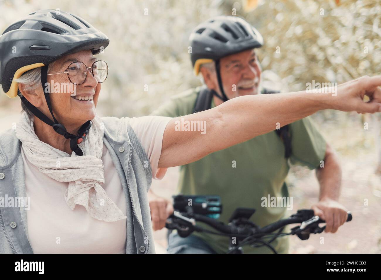 Zwei glückliche alte ältere Menschen genießen und gemeinsam Fahrrad fahren, um im Freien fit und gesund zu sein. Aktive Senioren, die Spaß beim Training in der Natur haben. Porträt eines alten Mannes, der mit seiner Frau lächelt und auf einer Fahrradtour ist. Frau zeigt etwas an und schaut es an. Stockfoto