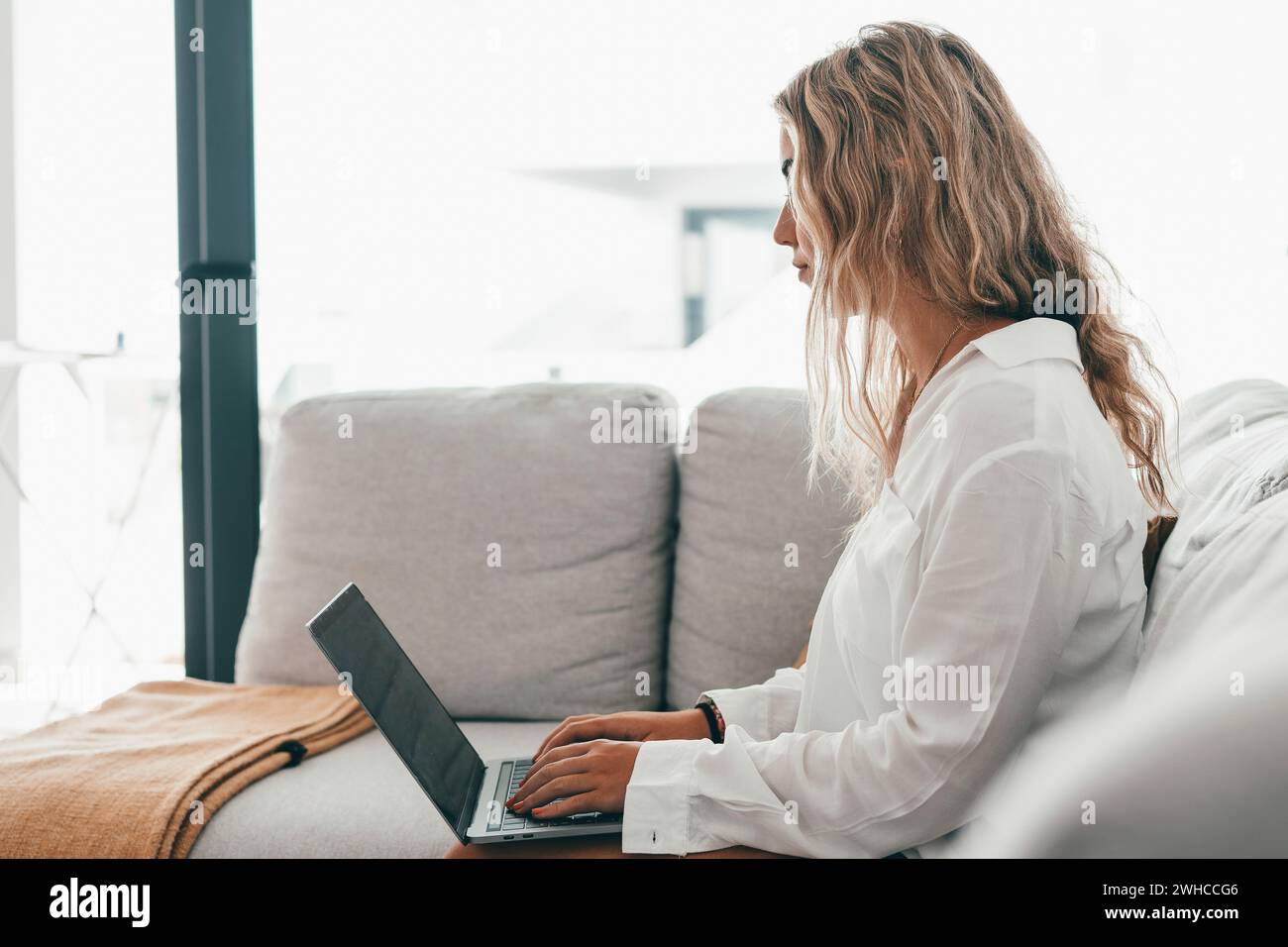 Porträt einer jungen attraktiven blonden Frau, die einen Laptop-pc auf der Couch benutzt und zu Hause im Internet surft. Working Online Concept Lifestyle Stockfoto