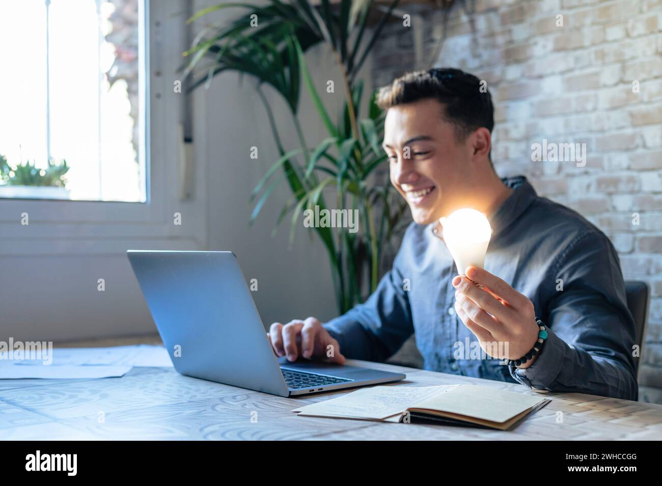 Nahaufnahme von männlichen Mitarbeitern Arbeit am Computer Halten helle Glühbirne Erhalten Sie eine brillante Geschäftsidee. Geschäftsmann oder Mitarbeiter fühlen sich motiviert mit einem erfolgreichen Startup-Projekt im Büro. Innovationskonzept. Stockfoto