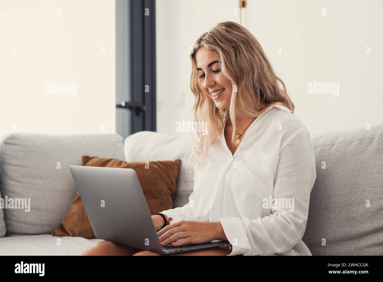 Porträt einer jungen attraktiven blonden Frau, die einen Laptop-pc auf der Couch benutzt und zu Hause im Internet surft. Working Online Concept Lifestyle Stockfoto