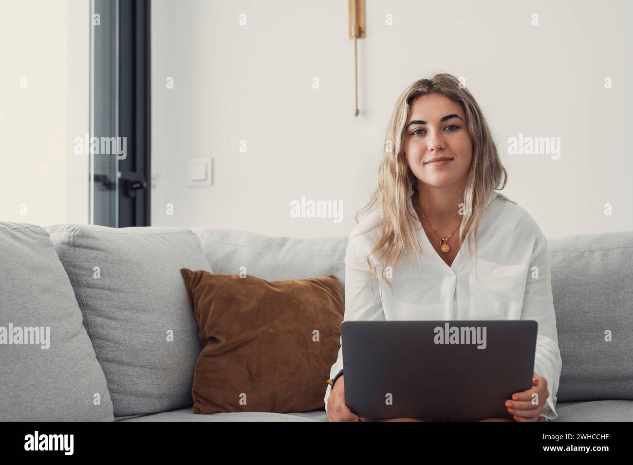 Porträt einer jungen attraktiven blonden Frau, die einen Laptop-pc auf der Couch benutzt und zu Hause im Internet surft. Arbeiten online lächelnd in die Kamera schauen Stockfoto