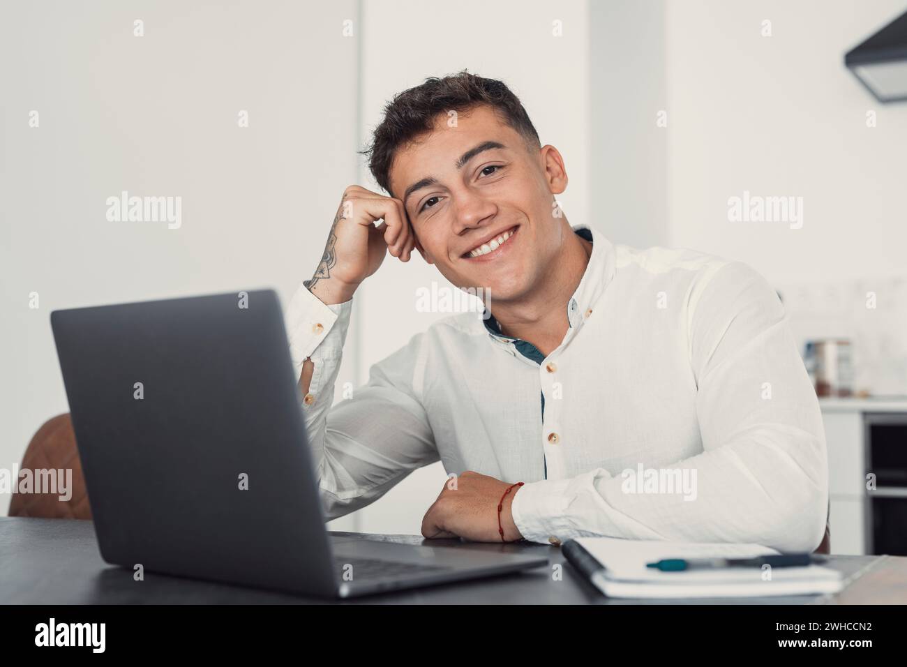 Gut aussehender Millennial Büroangestellter mit Brille am Schreibtisch vor dem Laptop und lächelnd in die Kamera. Erfolgreicher Mitarbeiter, Karrierefortschritt und Chancen, Eigentümer eines prosperierenden Geschäftskonzepts Stockfoto