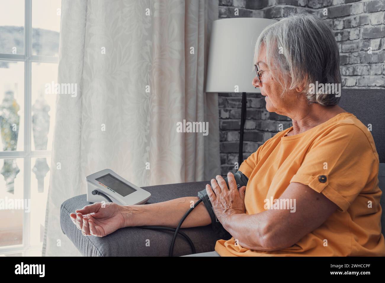 Ältere Frau messen hohen niedrigen Blutdruck Test Halten mit medizinischen digitalen elektronischen Meter sitzen auf Sofa zu Hause, Herzkrankheit Atherosklerose Prävention, Hypotonie Hypertonie Konzept Stockfoto